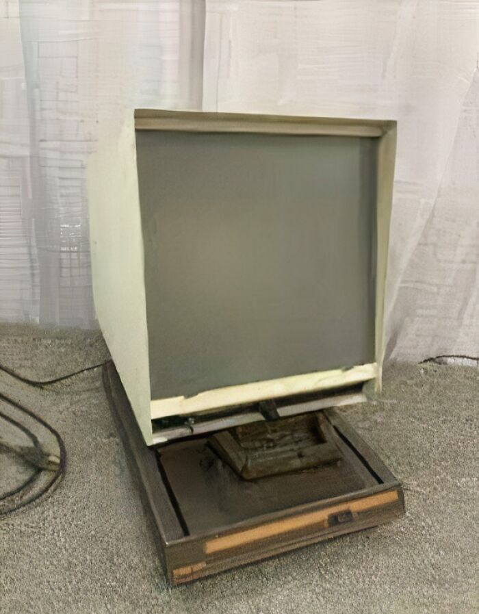 Starý počítačový monitor na podstavci s káblami v pozadí. Vintage technológia na šedom koberci.