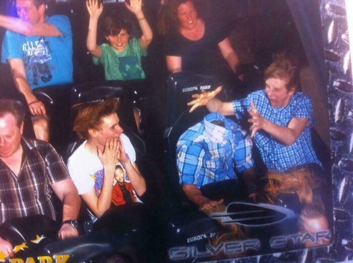 Skupina ľudí zažíva napínavú jazdu na horskej dráhe v parku, jeden sedadlový pasažier sa zdá byť neviditeľný.