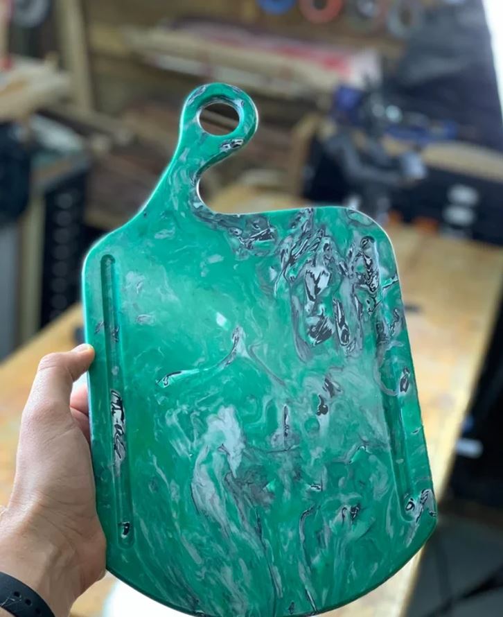 Zelená rezacia doska s mramorovým vzorom v ruke na dielenskom pozadí.