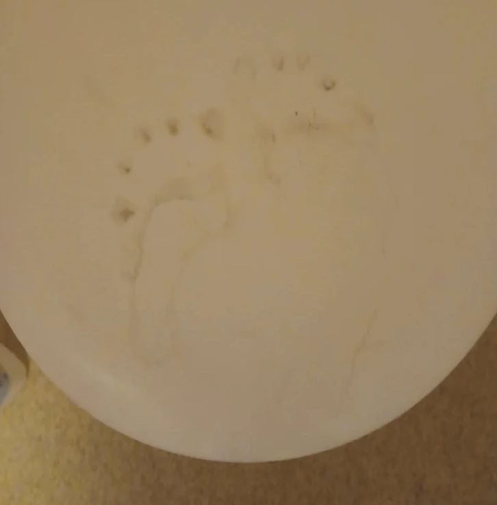 Odtlačok bosého chodidla na keramickej miske v kúpeľni, jemné obrysy prstov na bledom povrchu.