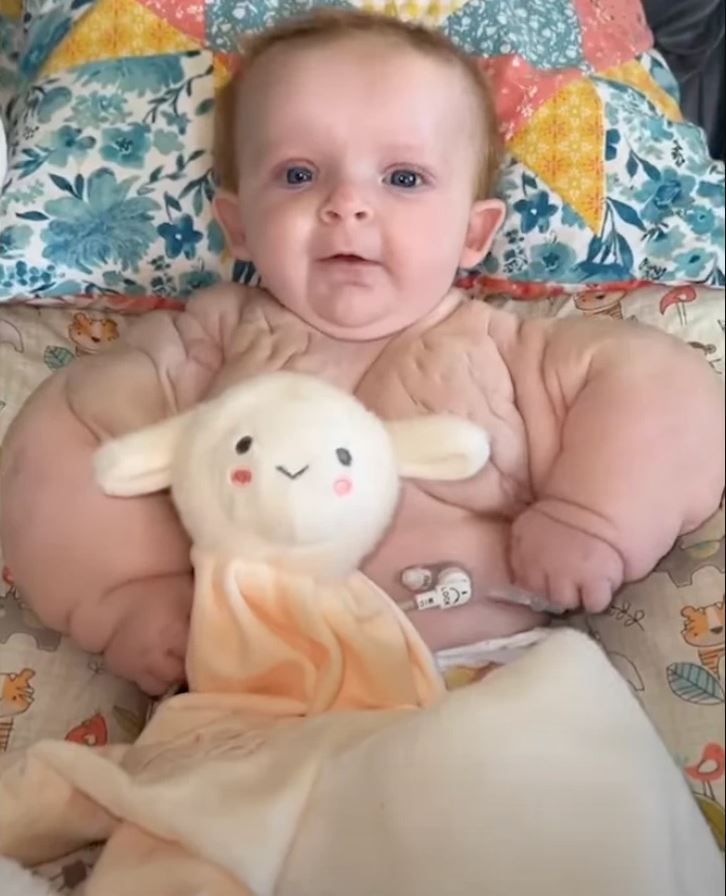 Dieťa leží s plyšovou hračkou na farebnej deke so vzorom kvetov a trojuholníkov.