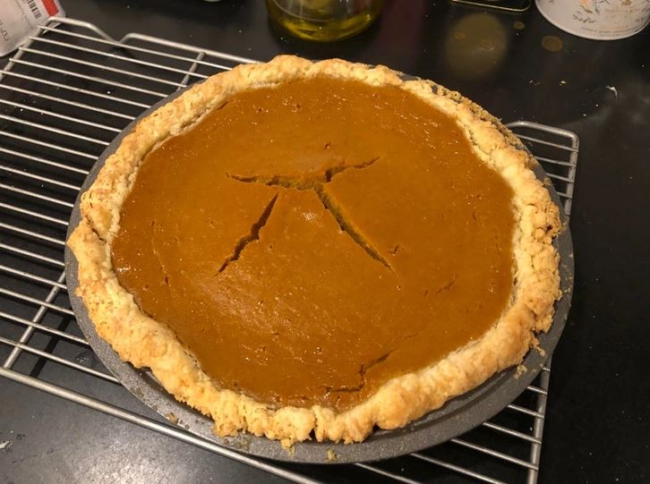 Domáca tekvicová torta s jemne popraskaným povrchom na chladiacej mriežke v kuchyni.