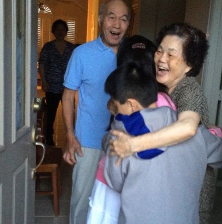 Starí rodičia s úsmevom objímajú vnúčatá vo vchodových dverách.