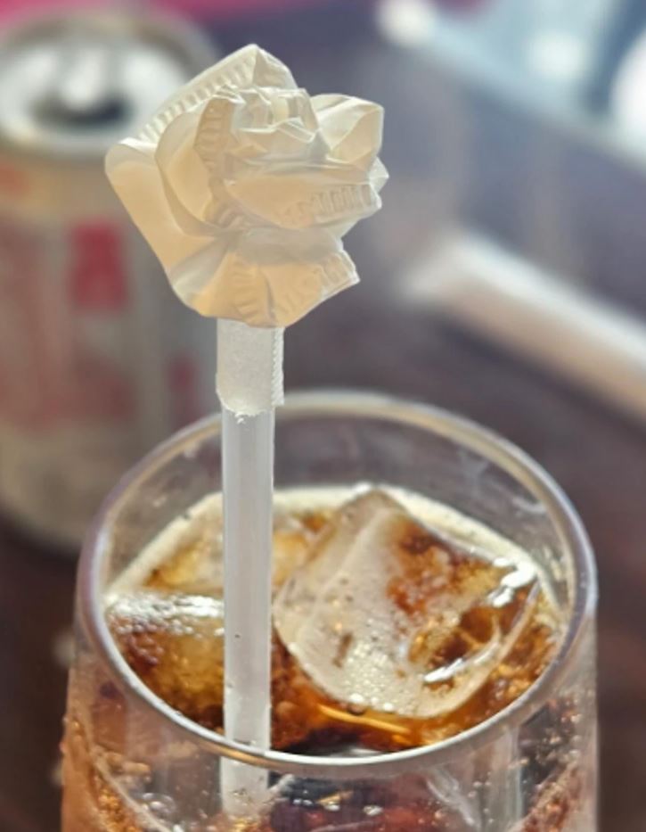 Slamka s dekoráciou z obrúska v pohári s ľadom a nealkoholickým nápojom, pozadie rozmazané.