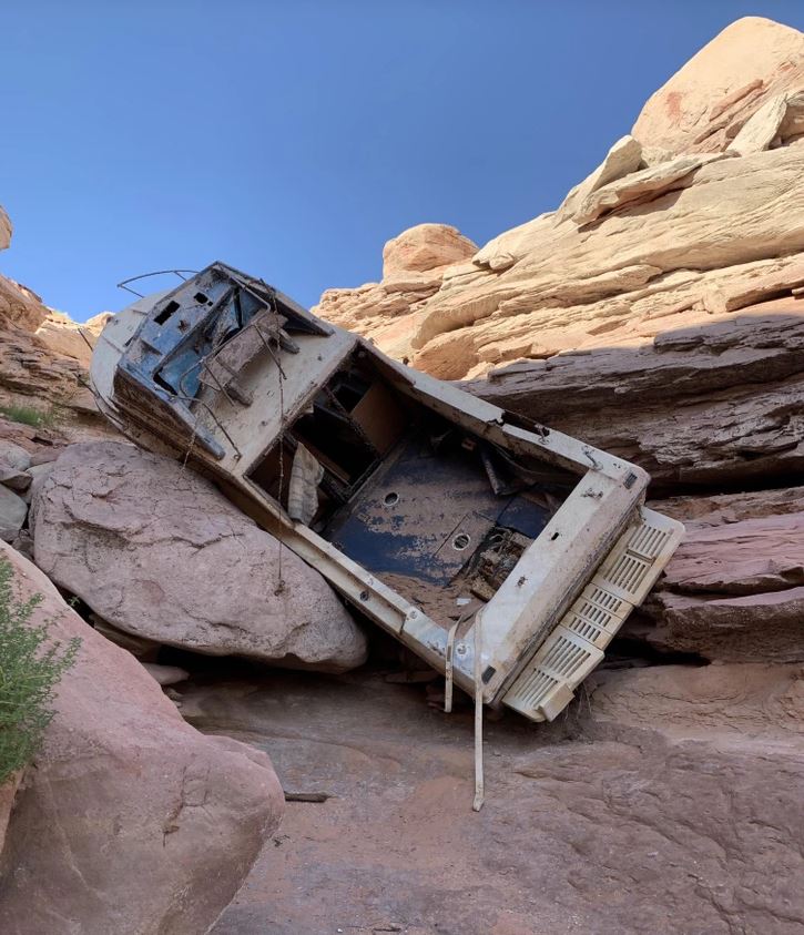Staré auto zakliesnené medzi skalami v púštnom kaňone pod modrou oblohou.