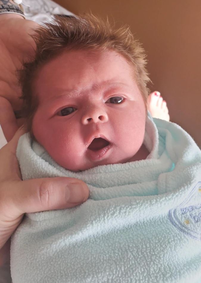 Bábätko zabalené v mäkkej deke s otvorenými ústami a roztomilým výrazom v očiach.