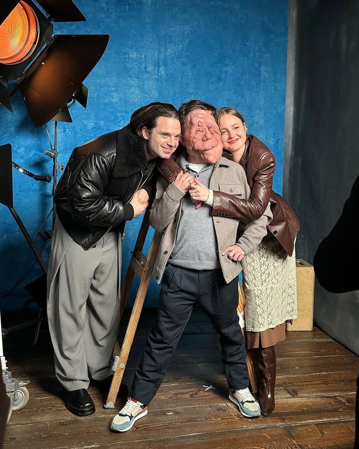 Žena a dvaja muži v priateľskom objatí pred modrým pozadím a filmovým svetlom.