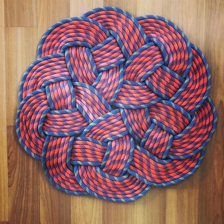 Zložité pletené lanové podložie na drevenej podlahe, kombinácia modrých a červených vzorov.