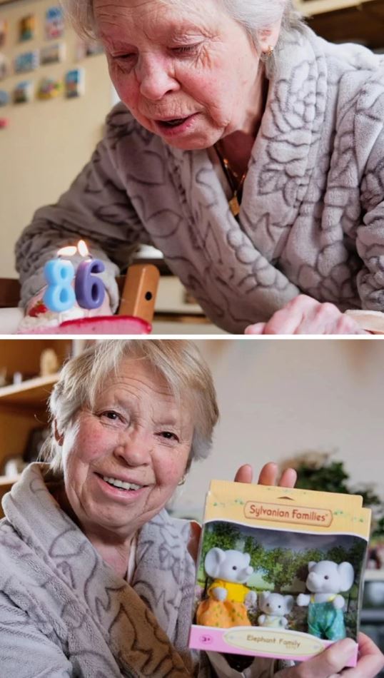Staršia žena v župane sfukuje sviečky na torte s číslom 86, drží hračku Sylvanian Families - rodinka slonov.