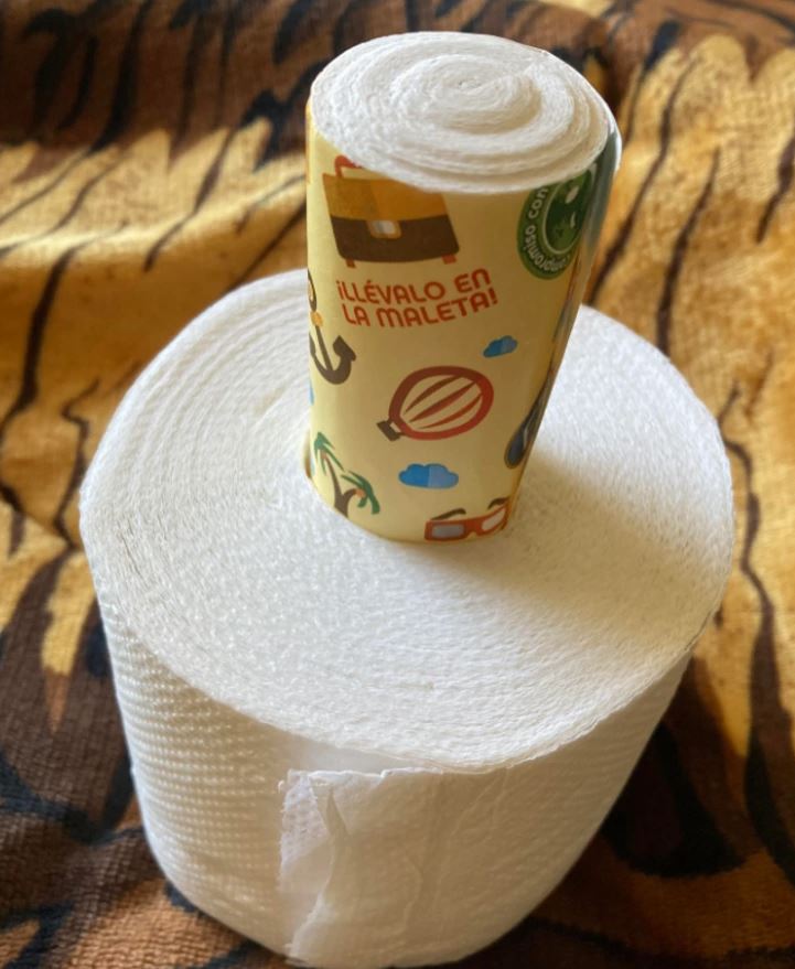 Cestovná rolka toaletného papiera s farebným obalom leží na väčšej rolke na zvieracom vzore látky.