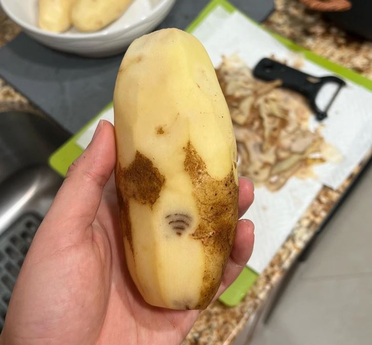 Olúpaná zemiak s hnedými škvrnami a čiernou chybičkou, držiak na šúpanie v pozadí.