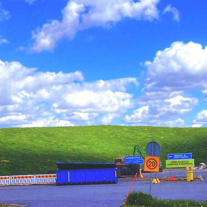 Stavenisko s kontajnerom a obmedzením rýchlosti na 20 km/h na pozadí zeleneho kopca a modrej oblohy.