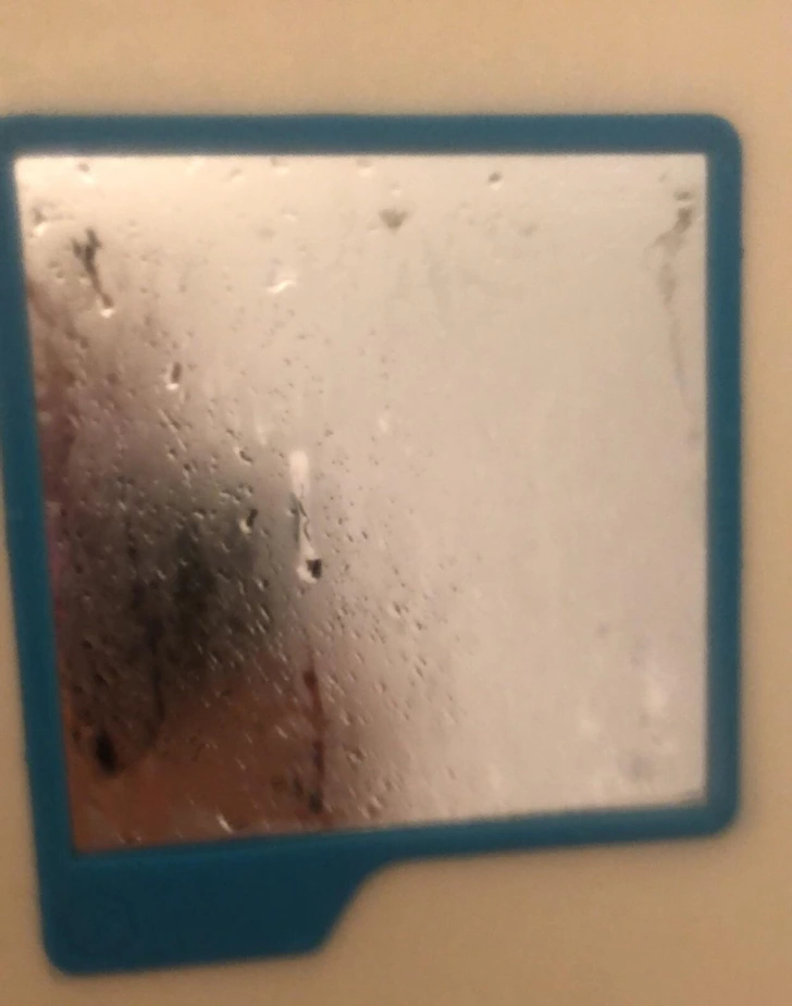 Zahmlené zrkadlo v modrom ráme s kvapkami vody, kúpeľňová atmosféra po sprchovaní.