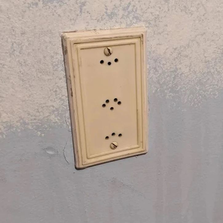 Starý biely vypínač na štruktúrovanej stene, pravdepodobne zastaraný dizajn domácnosti.