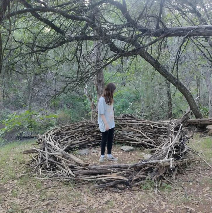 Osoba stojí v lese vo vnútri kruhu z vetiev, obklopená prírodou.