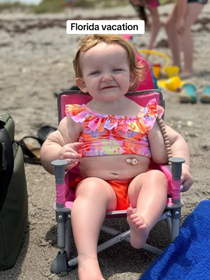 Dieťa v plavkách sedí na pláži na Floride, usmieva sa v slnečnom počasí.