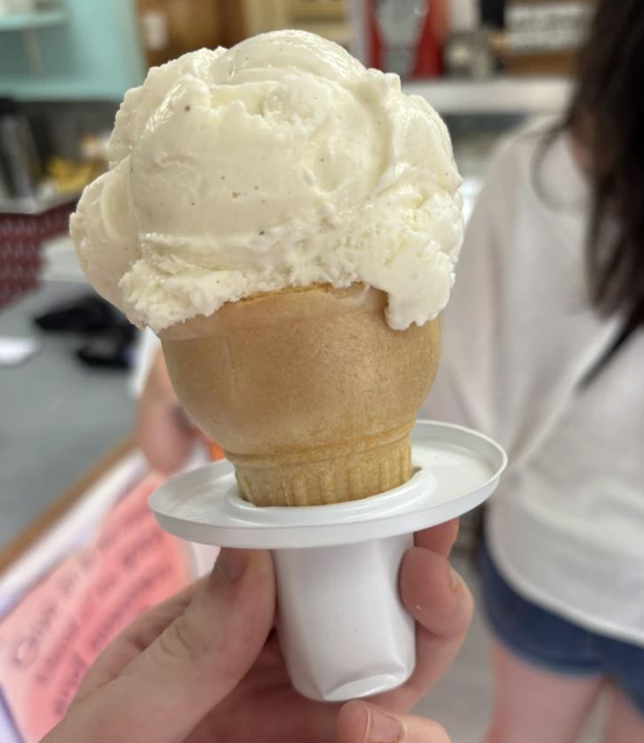 Vanilková zmrzlina na kornútku s plastovou držiakovou základňou, pozadie rozmazané.