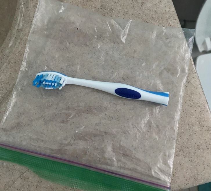 Zubná kefka leží na plastovom obale na béžovom povrchu v kúpeľni.