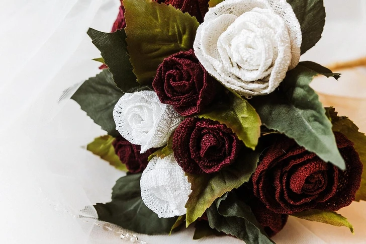 Kytica z látkových ruží v bielych a bordových odtieňoch s bohatými zelenými listami.