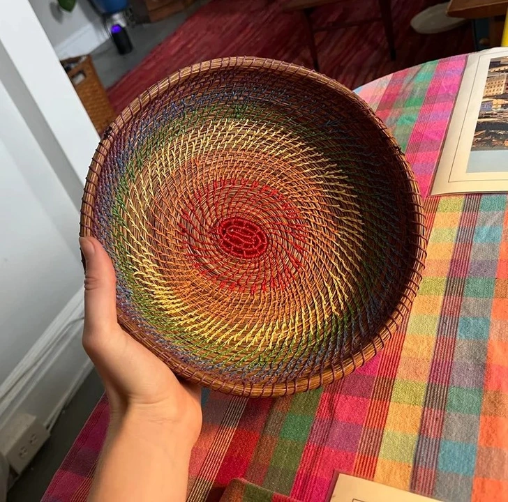 Farebný pletený košík držiaci v ruke, položený na pestrofarebnom stole.