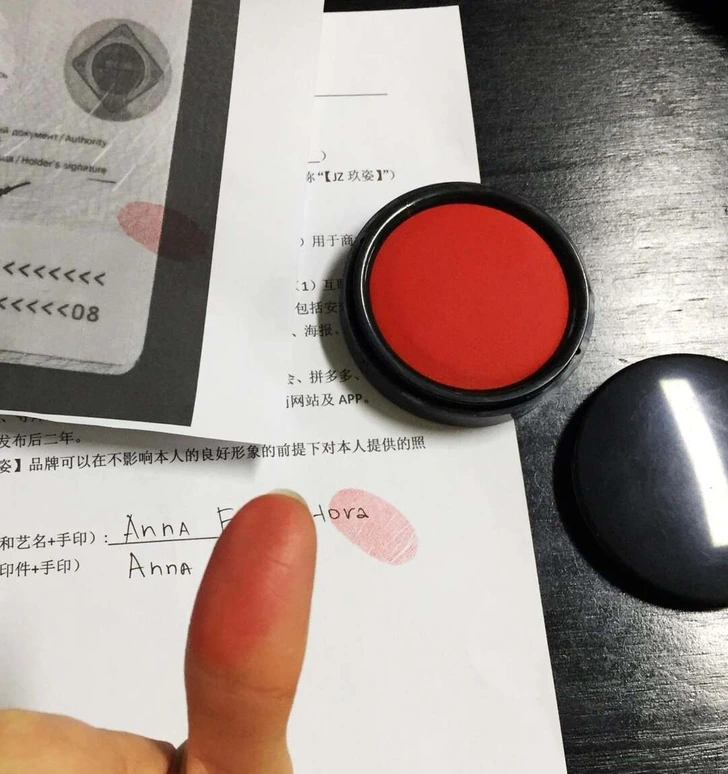 Osoba s otlačkom prsta a pečiatkovou poduškou podpisuje dokument na tmavom stole.