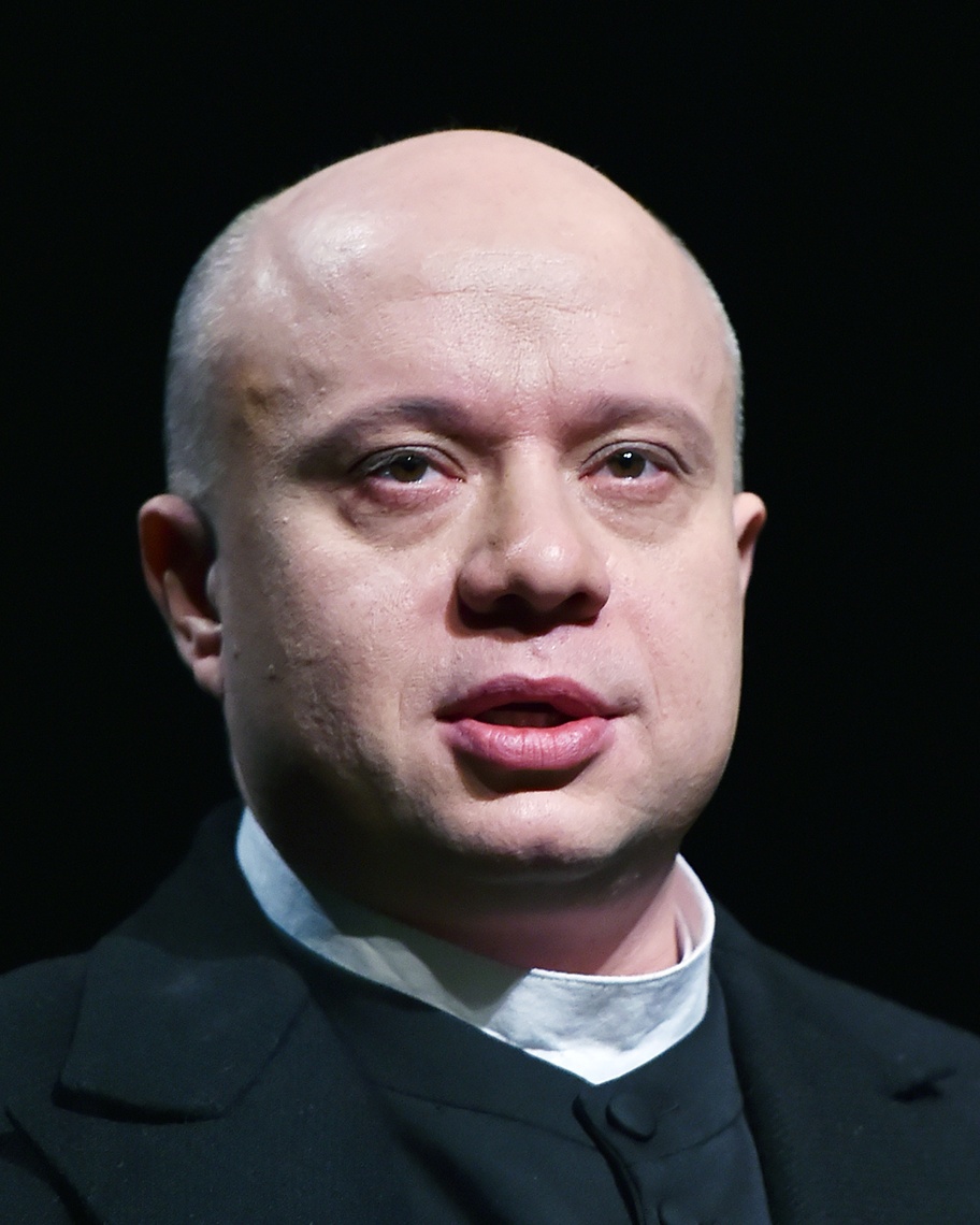 Osoba v čiernom oblečení na tmavom pozadí, vyjadrujúca intenzívny výraz tváre.