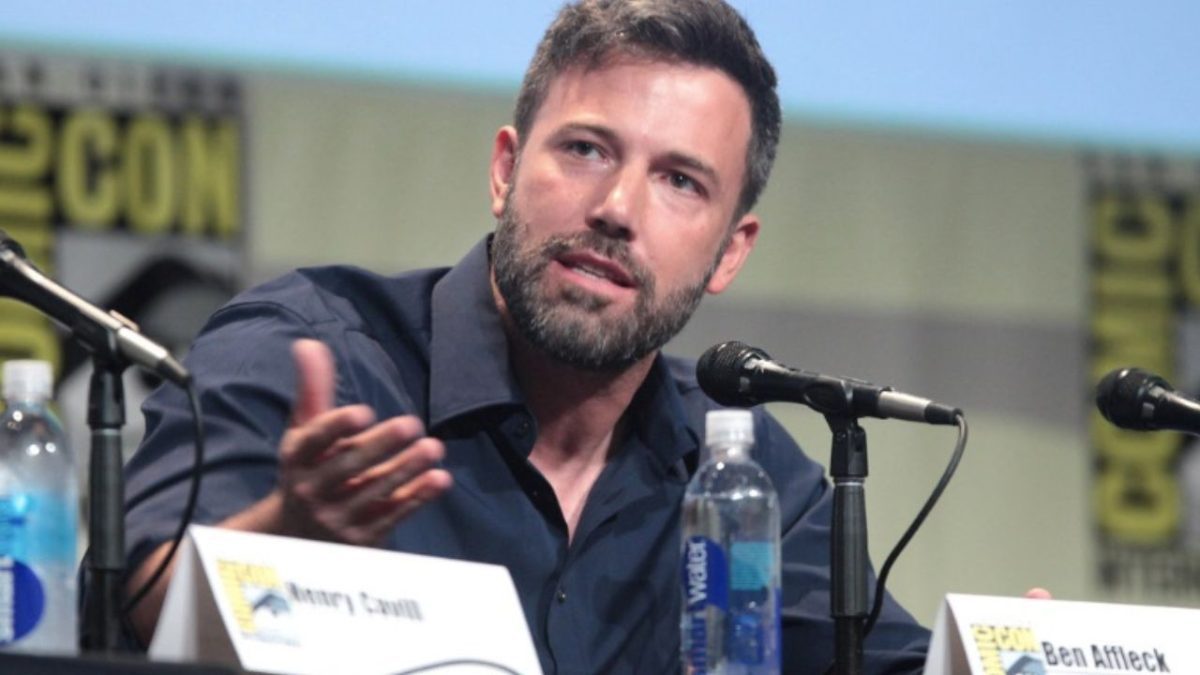 Muž pri mikrofóne na konferencii diskutuje, okolo sú fľaše vody a iné mikrofóny.