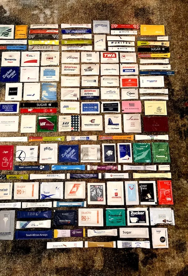Kolekcia balíčkov cukru s logami rôznych leteckých spoločností rozložená na zemi.