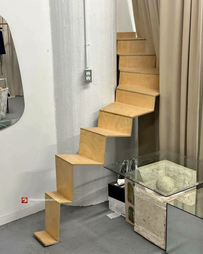 Drevené úzke schodisko s moderným dizajnom v interiéri vedľa skleneného stolíka s betónovou kockou.