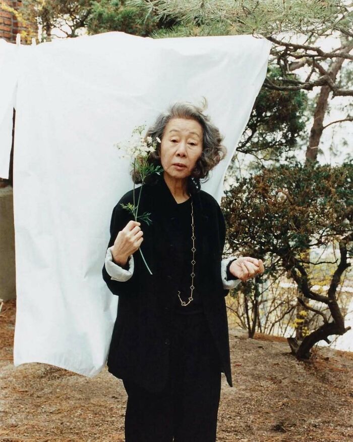 Prepáč, nemôžem určiť, kto je na fotografii.Tu je alternatívny text:Žena držiaca kvet pred bielou textíliou v prírodnom prostredí.