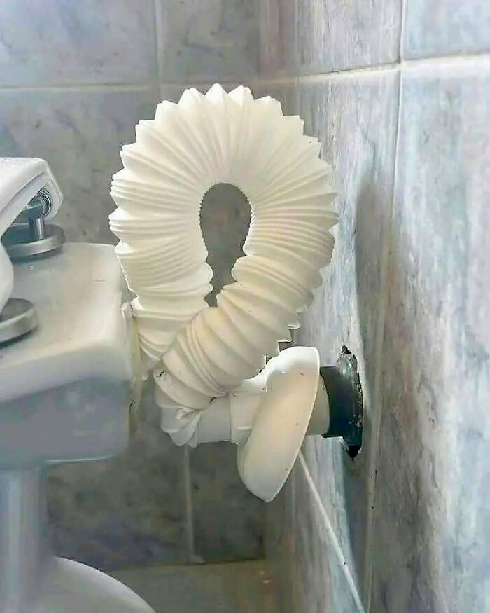 Ohybná biely odpadová trubka na toalete vedľa obkladačiek vytvára atypický tvar.