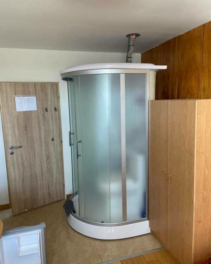 Sprchový kút umiestnený v izbe medzi drevenou skriňou a dverami, moderné a netradičné riešenie priestoru.