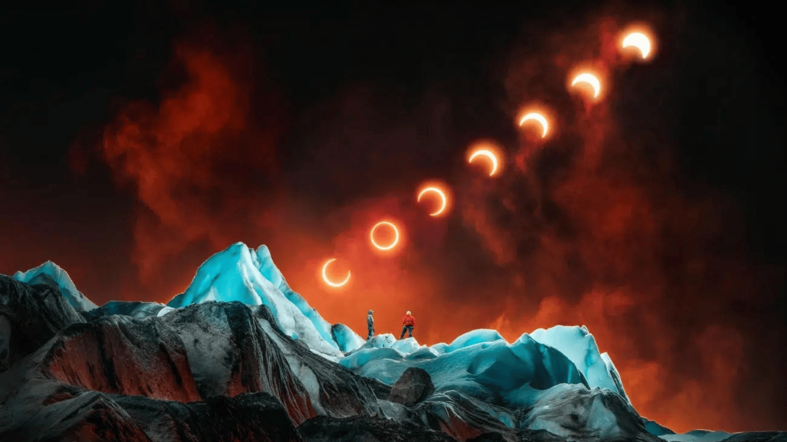 Dve osoby na ľadovej hore sledujú postupné zatmenie slnka na dramatickej oranžovej oblohe.