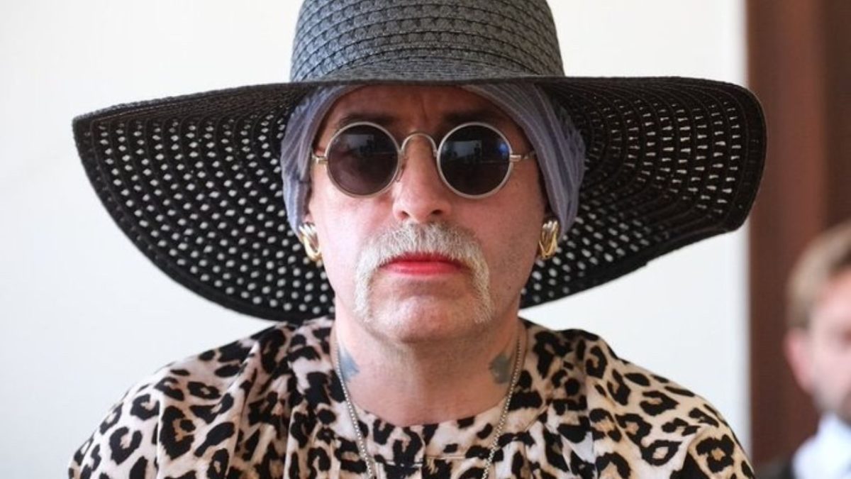 Osoba v klobúku a leopardom vzore, nosiaca slnečné okuliare, pôsobí extravagantným a výrazným dojmom.