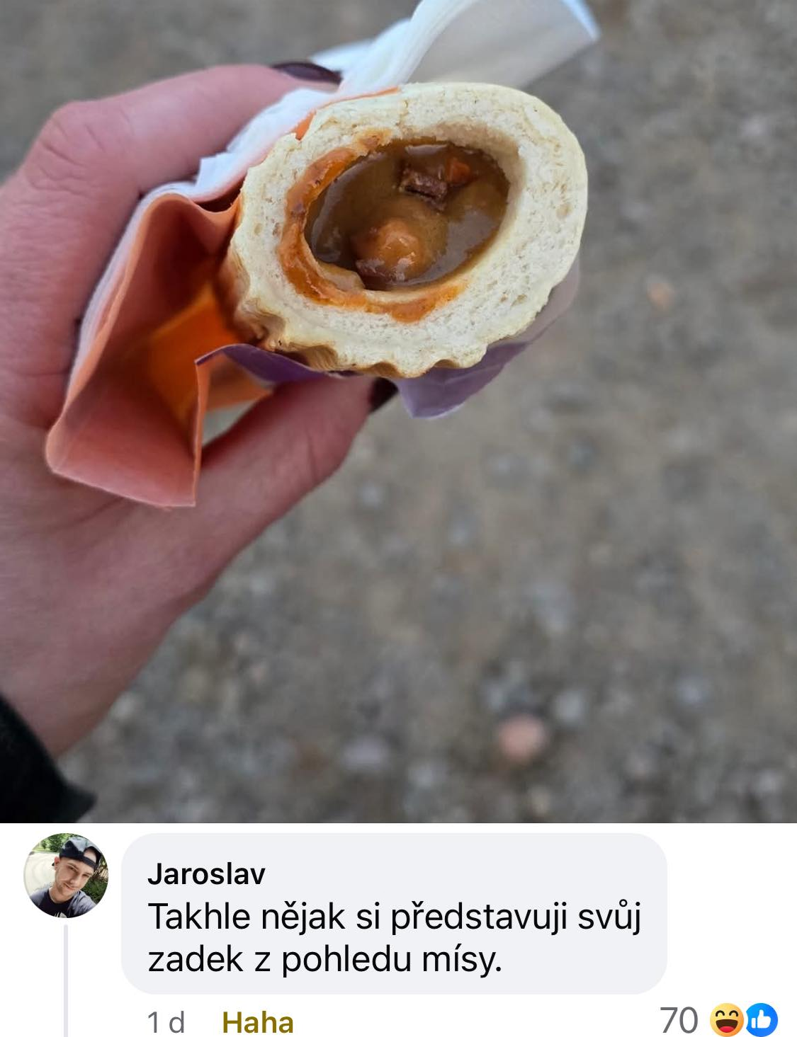 Osoba drží pečivo plnené omáčkou a kúskami jedla, so zábavným komentárom pod obrázkom.