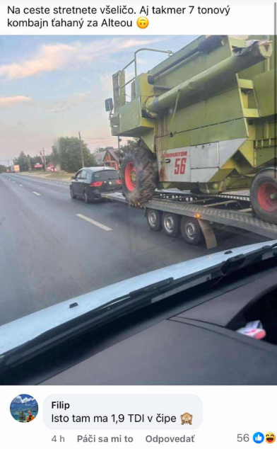 Na ceste je auto ťahajúce veľký kombajn na prívesnom vozíku.