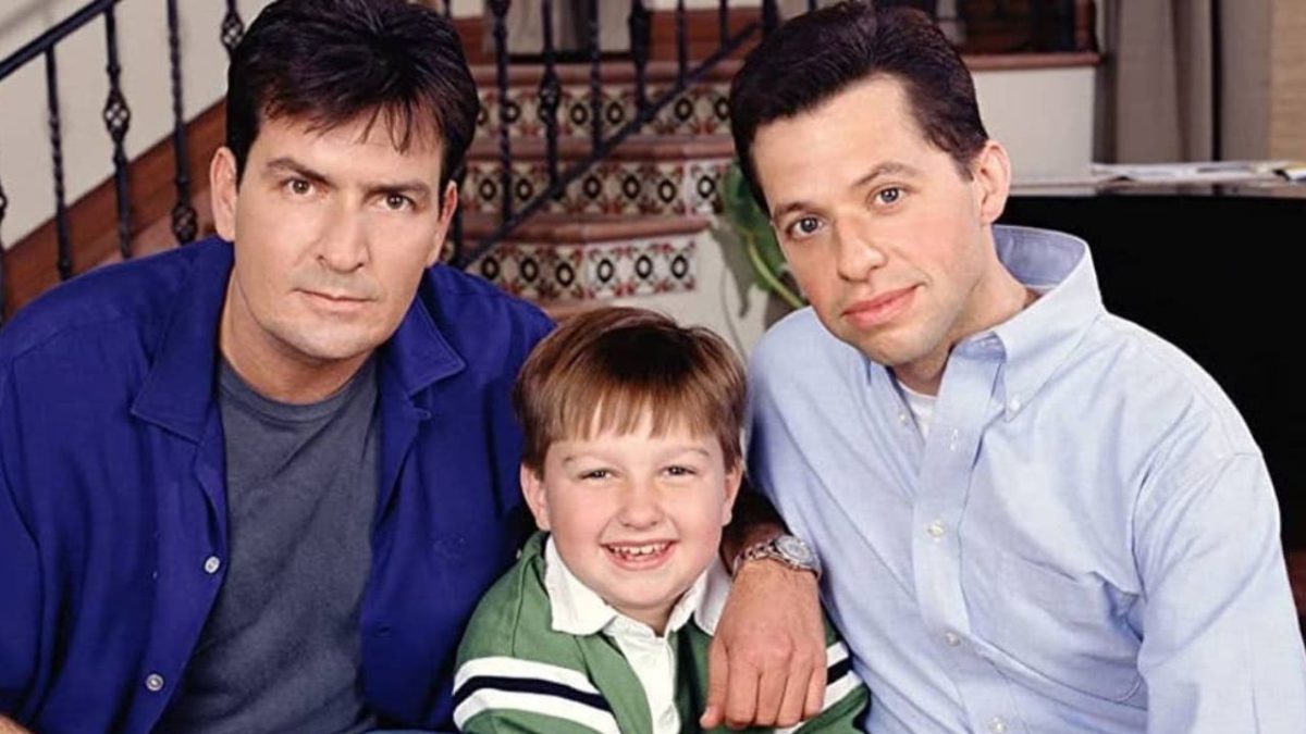 Trojica mužov sediacich na schodoch s úsmevom na tvárach, oblečených v neformálnom oblečení.