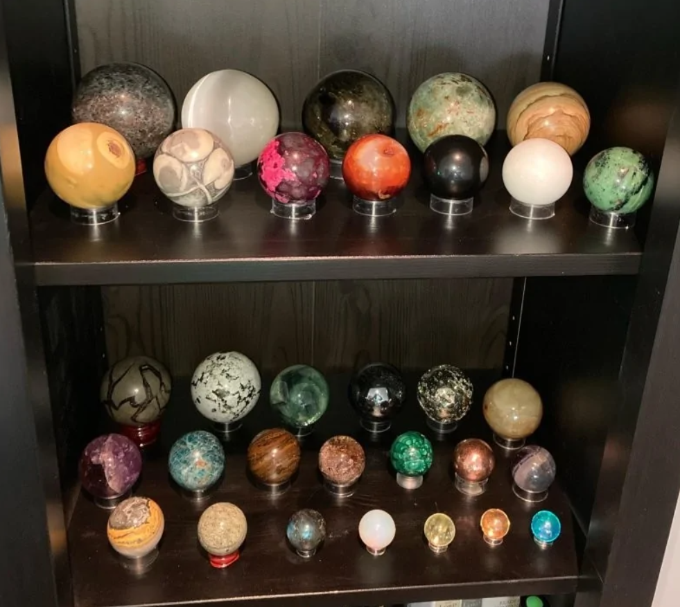 Rôznofarebné minerálne gule vystavené na poličke v tmavom drevenom regáli.