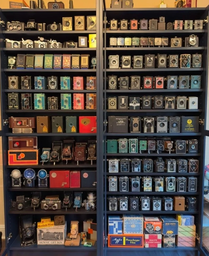 Polica s farebnými vintage kamerami a optickým príslušenstvom vystavenými v zbierke.