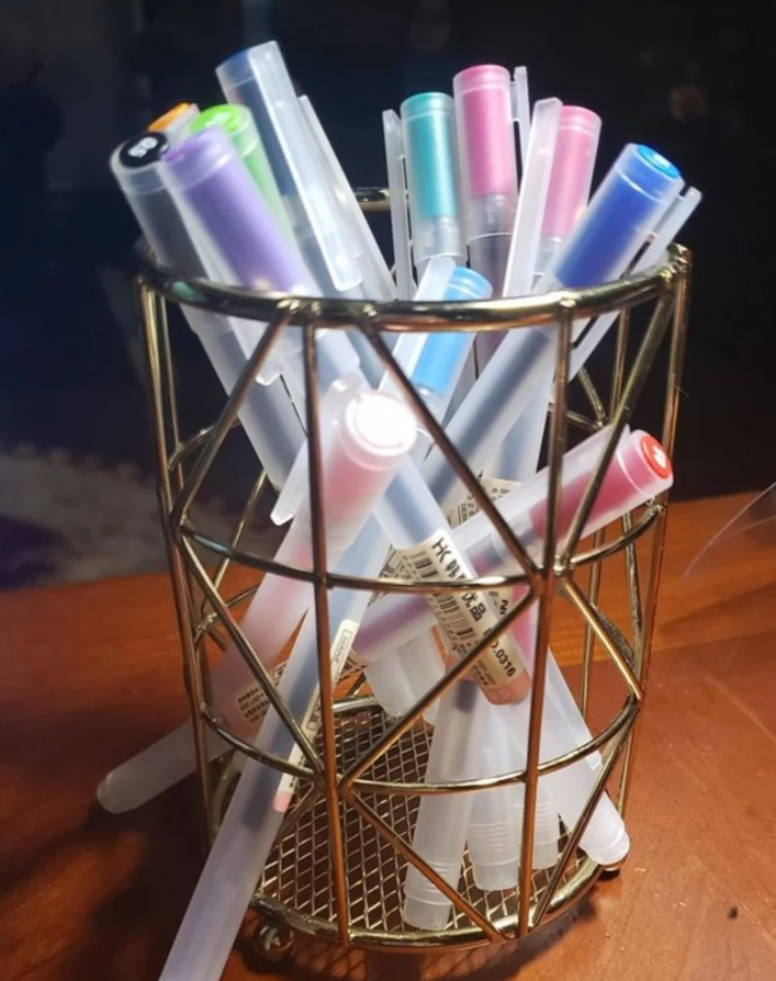 Farebné perá v zlatej drôtenej nádobe na drevenom stole.