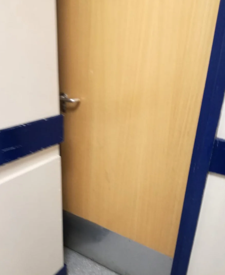 Drevené dvere s kovovou kľučkou, otvorené vedúce do chodby s modrými a bielymi stenami.