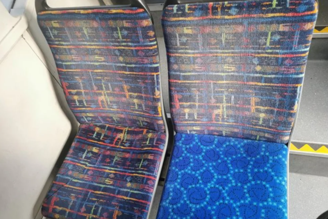 Dve sedadlá v autobuse s rôznym vzorom textilu, jeden s modrým dizajnom, druhý s farebným geometrickým vzorom.