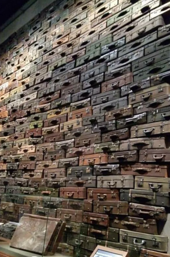 Stena pokrytá historickými kuframi, rôzne farby a veľkosti, symbolizuje príbehy z minulosti.