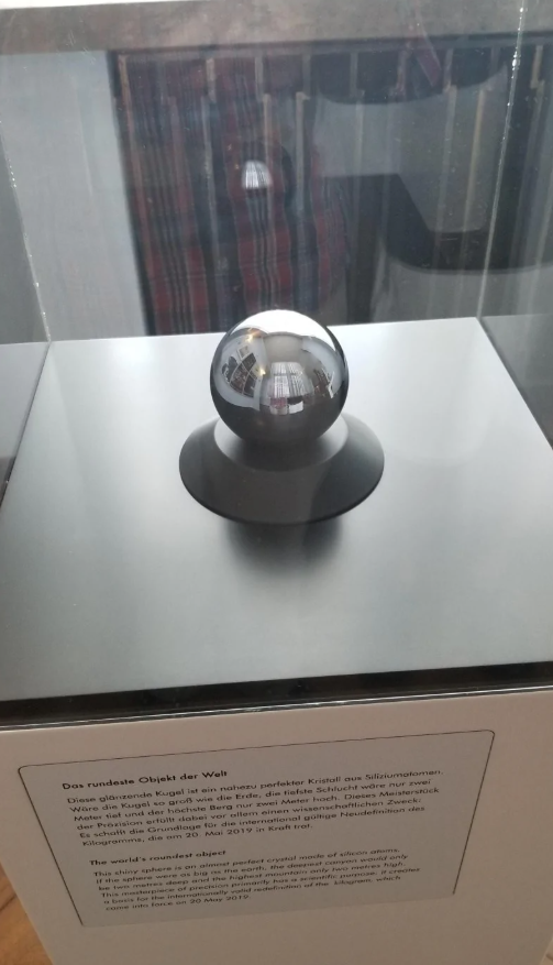 Lesklá guľa na podstavci vystavená v sklenenej vitríne s popisom o jej unikátnych vlastnostiach.