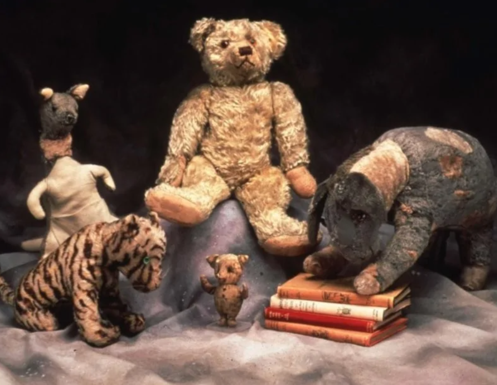Staré vypchaté zvieratká sedia spolu okolo kníh, vrátane medveďa, tigra a slona, na tmavom pozadí.