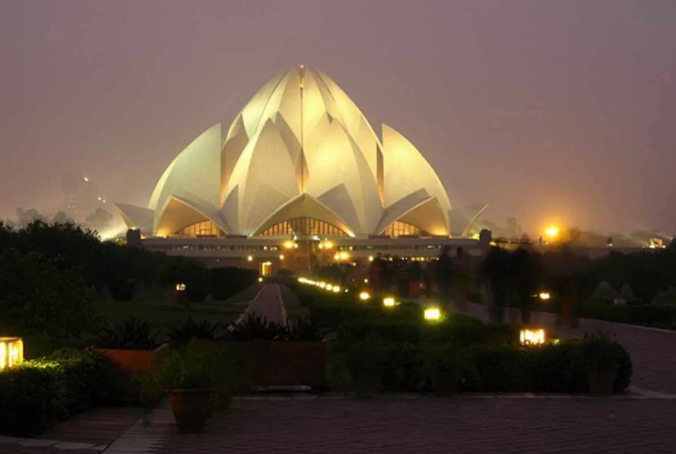 Osvetlený Lotusový chrám v Dillí za súmraku, v popredí cestička a zeleň, symbol moderného indického dizajnu.