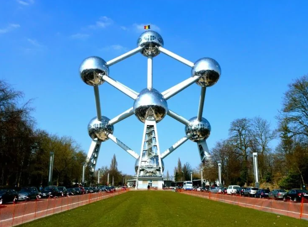 Ikonické Atomium v Bruseli pod modrou oblohou, obklopené stromami a návštevníkmi.