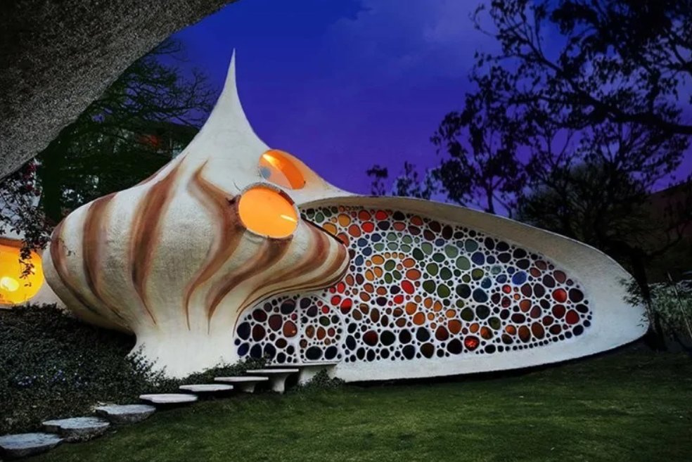 Futuristický dom v tvare ulity s farebnými oknami a nočnou oblohou v pozadí.