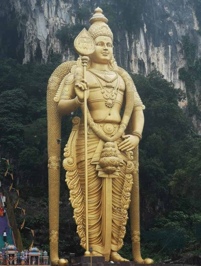 Zlatá socha boha v Batu jaskyniach, Malajzia, obklopená prírodou a schodiskom plným farebného zdobenia.