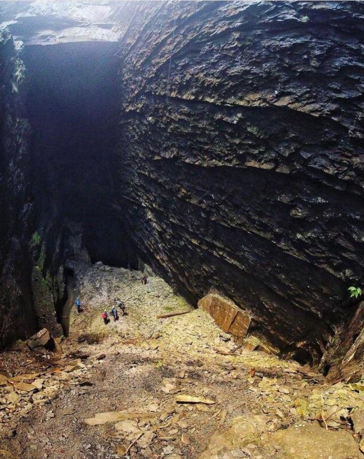 Skupina turistov objavuje impozantný vstup do skalnatej jaskyne, obklopená vysokými skalami.